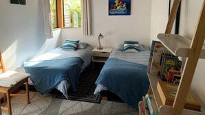A bedroom with two beds, a window with curtains, a painting on the wall, and a bookshelf with books. - Treetop Hideaway - Taupo Holiday Home (Taupo Central)