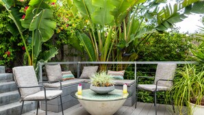 Un espace extérieur aménagé avec une table ronde, des chaises rembourrées et un pot de fleurs.