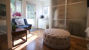 Un salon moderne avec un canapé bleu, une table basse en bois et un pouf capitonné. Une grande fenêtre laisse entrer la lumière naturelle et offre une vue sur la verdure environnante.