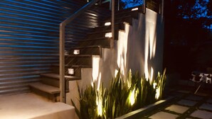 Un escalier moderne avec une rampe en métal, menant à un bâtiment doté d’une façade en verre.