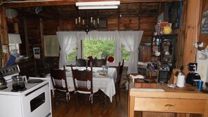 A rustic cabin interior with a dining area, wooden walls, a white stove, and a kitchen counter. - Classic Lakeside Maine Cottage (Sumner)