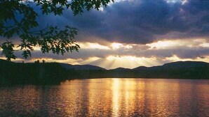 A calm lake at sunset with mountains in the background and a tree branch in the foreground. - Classic Lakeside Maine Cottage (Sumner)