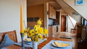 A dining area with a wooden table set for two, a vase with yellow flowers, and a tall candle. - Vacation apartment Hofblick - Ferienhof Börsby - Holiday apartment Hofblick (Pommerby)