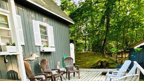 A wooden deck with outdoor seating, a small table, and a building with shutters. - An Onekama gem. Short walk to a quiet beach. (Onekama)