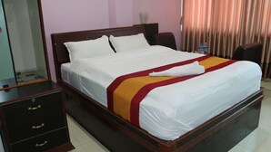 Una cama bien hecha con cubrecama blanco y rojo, un cabecero de madera y una mesita de noche con cajones.