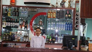 Zona de bar con diversas botellas de licores, un monitor de computadora y una caja registradora.