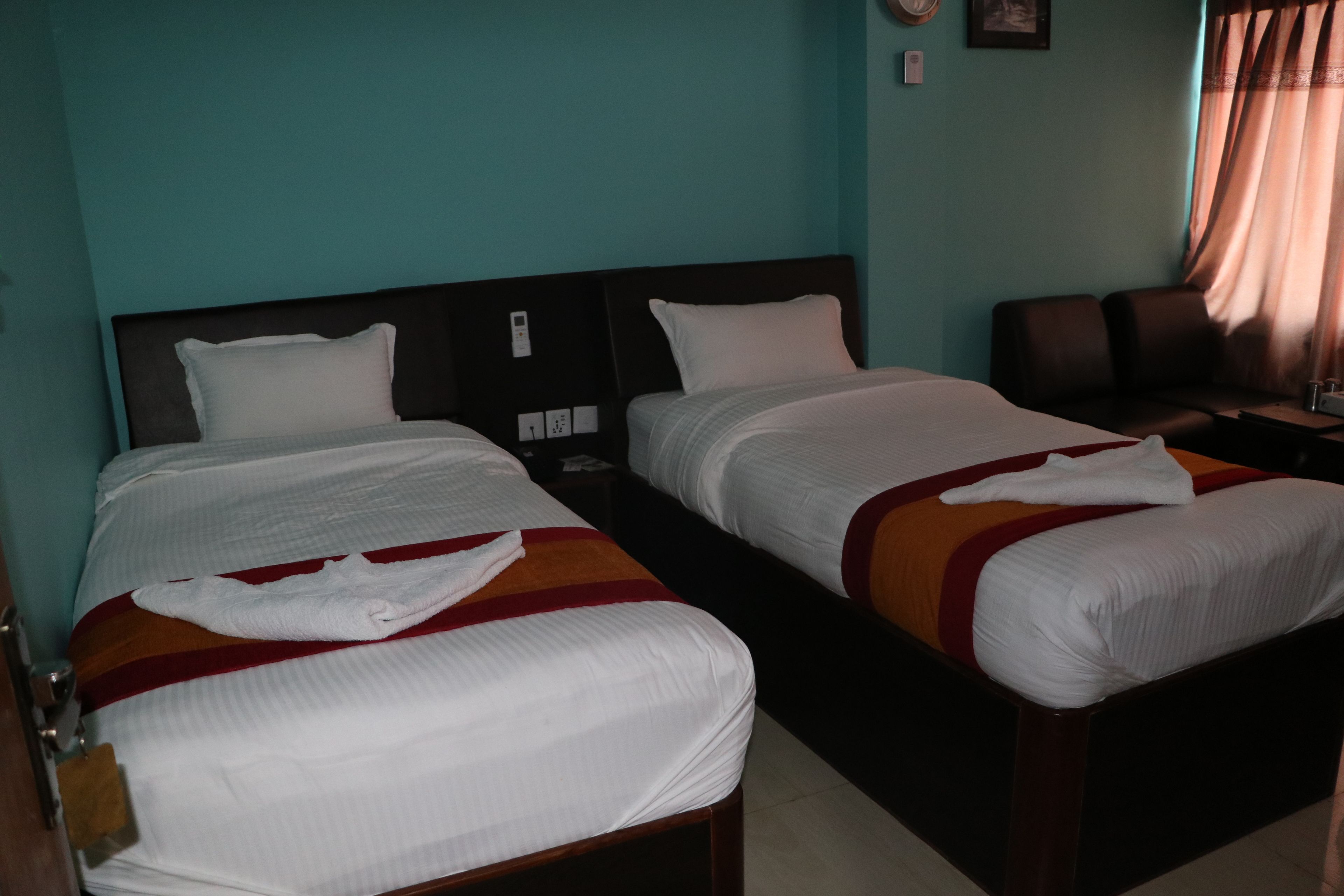 A hotel room with two single beds, a wooden headboard, a nightstand, and a brown leather chair.