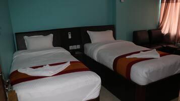 A hotel room with two single beds, a wooden headboard, a nightstand, and a brown leather chair.