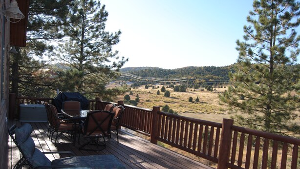 Terraza de madera con mobiliario exterior, con vistas a un paisaje boscoso.