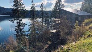 A lakeside cabin with a metal roof, surrounded by tall trees and a clear sky. - Waterfront house in Bayview! Boating, fishing, amazing views, 12mi to Silverwood (Bayview)