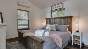 A bedroom with a wooden headboard, a bed with pillows, a bedside table with a lamp, and a sign above the bed. - Waterfront house in Bayview! Boating, fishing, amazing views, 12mi to Silverwood (Bayview)