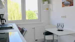 A modern kitchen with a built-in stove, a window with a view of greenery, a white radiator, and a small white table with a plant and a picture on the wall. - legendary germany (Bad Harzburg)