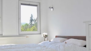 A bedroom with a large window, a bed with white bedding, a bedside table with a vase of flowers, and a wall-mounted light fixture. - legendary germany (Bad Harzburg)