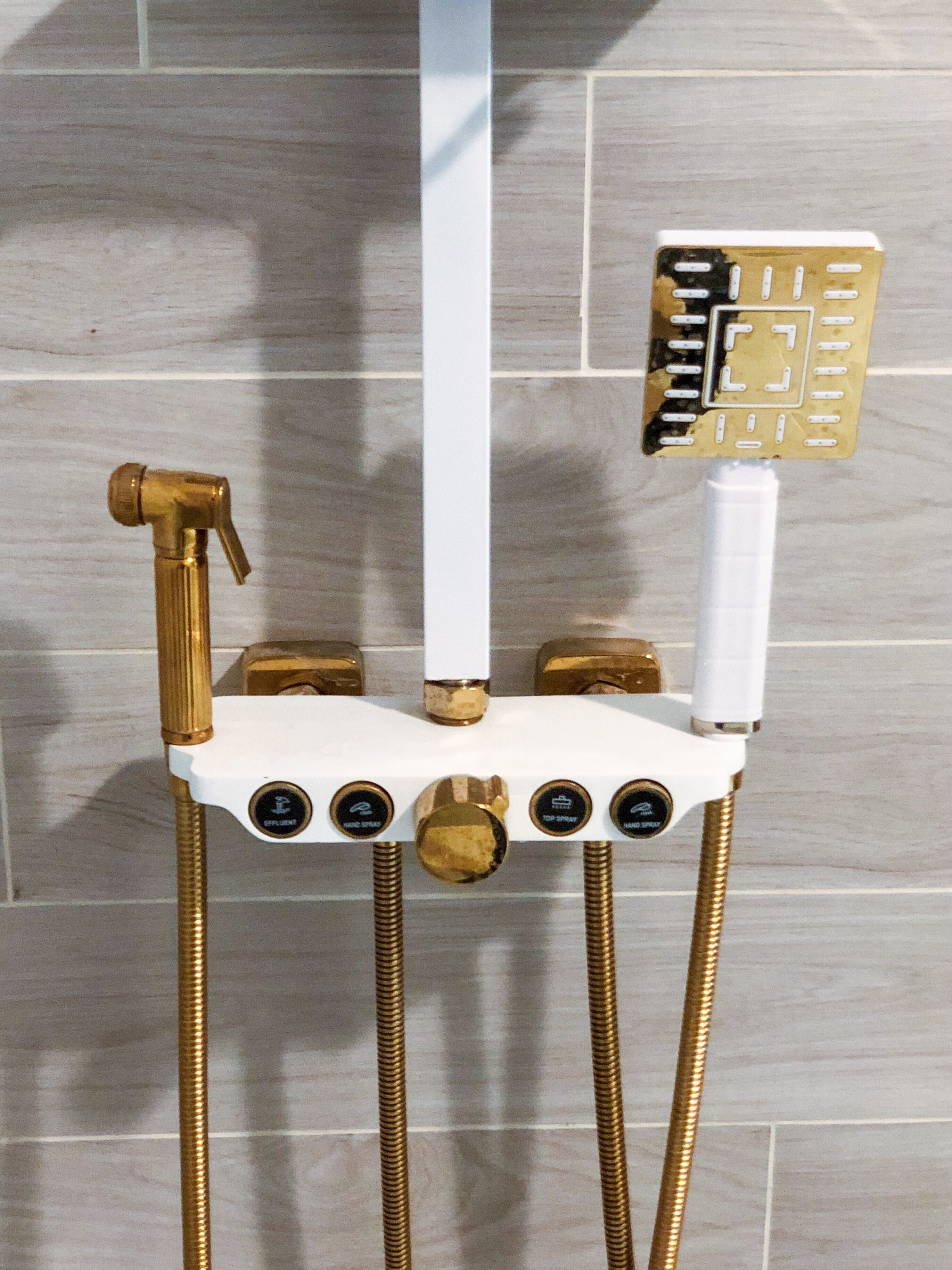 A shower unit with a gold faucet, a white control panel, and a gold showerhead.