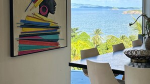 Una zona de dinar moderna amb un gran finestral que ofereix vistes al mar i vegetació.