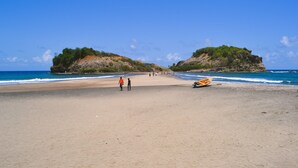 Una platja amb dues illes rocoses, una riba sorrenca i una barca petita.