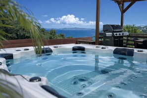 Un jacuzzi con vista al océano, una parrilla para barbacoa y una pérgola de madera.