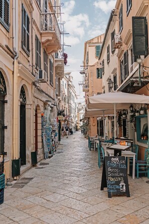 Une rue étroite bordée d’immeubles, de terrasses et d’un panneau indiquant les différents plats et boissons proposés.