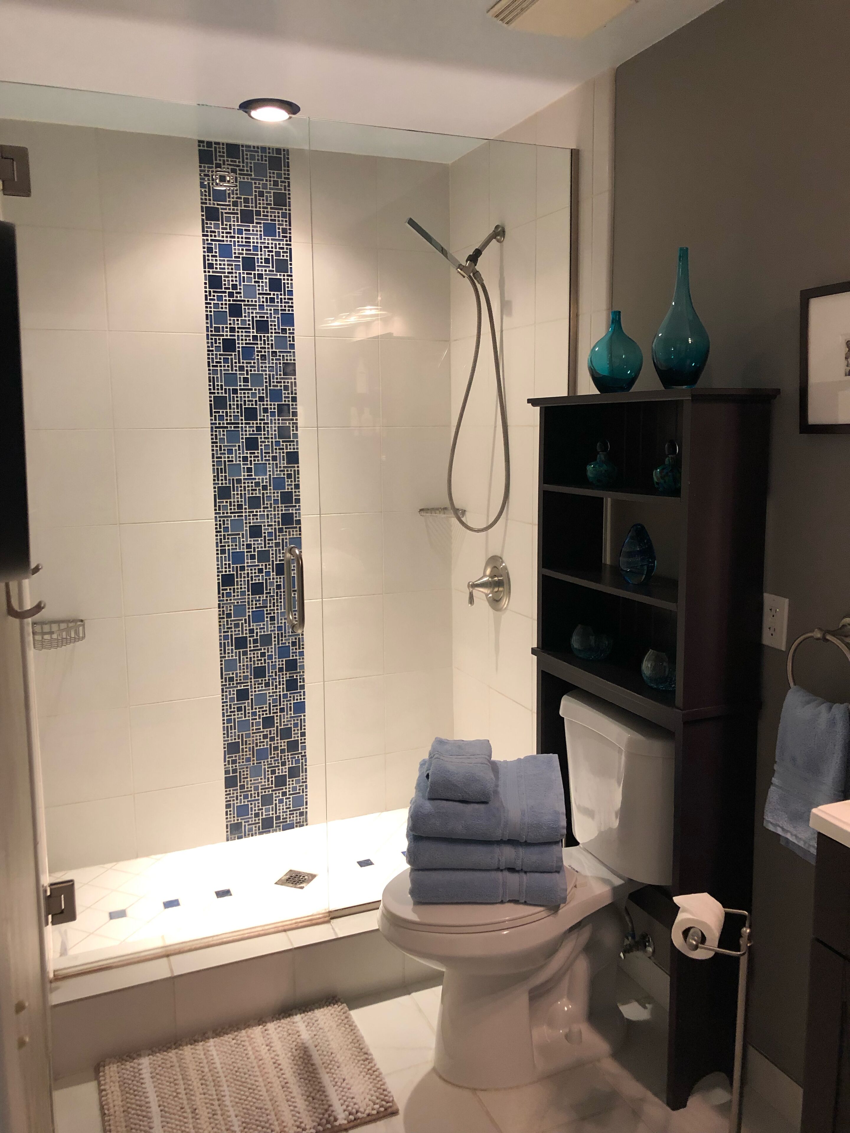 Et moderne badeværelse med en brusekabine med glasvægge, toilet og et vaskeskab med hylder.