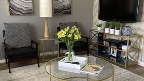 Een moderne woonkamer met een ronde glazen salontafel, twee banken, een televisie en decoratieve objecten.