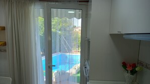 A room with a sliding glass door leading to a pool area, a white chair, a small table, a vase with flowers, and a stove. - Chalet with mountain views and private pool, ideal for families.  (viladecavalls)