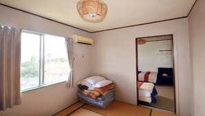 A room with a bed, a window with curtains, an air conditioning unit, and a woven light fixture. - Hotel Henza (Uruma)