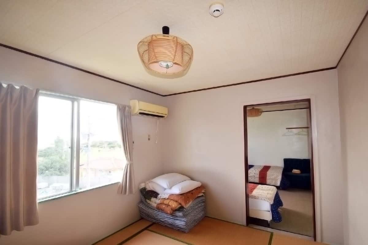 A room with a bed, a window with curtains, an air conditioning unit, and a woven light fixture.