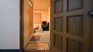 A hallway leading to a bedroom with a bed, a chair, and a television. - Hotel Henza (Uruma)