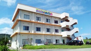 A multi-story building with a flat roof, air conditioning units, and a car parked in front. - Hotel Henza (Uruma)