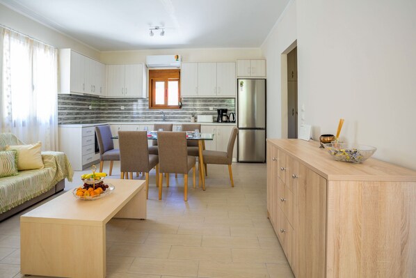 A modern kitchen with white cabinets, a stainless steel refrigerator, and a dining area with a wooden table and chairs.