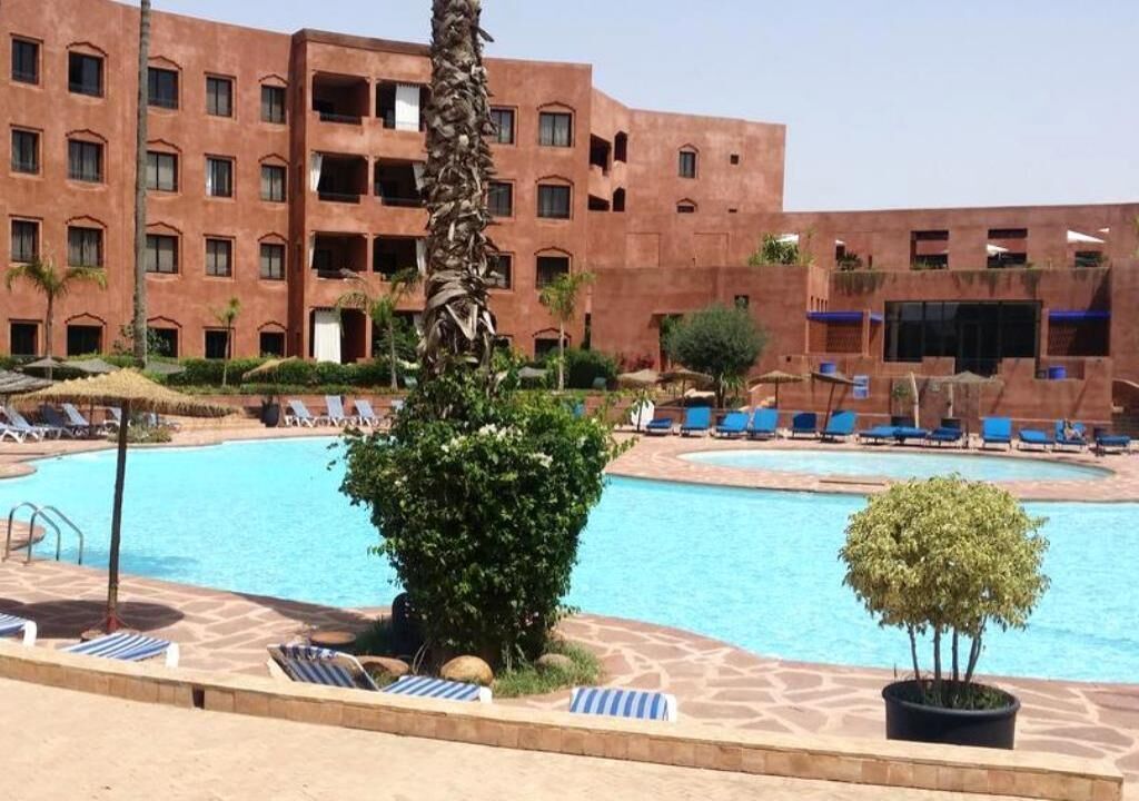 A hotel with a pool area, including lounge chairs and a palm tree.