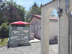 Un espace extérieur abrité, avec des sièges, un parasol rouge, une clôture en treillis blanc et un pilier en pierre.