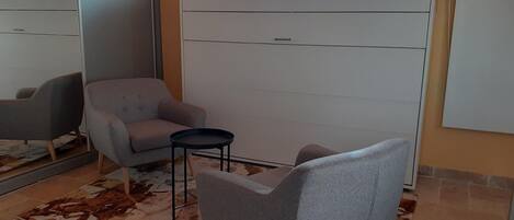 Relax in this stylish living room with a sofa, armchair, and coffee table, offering a view of the outside through the large window.