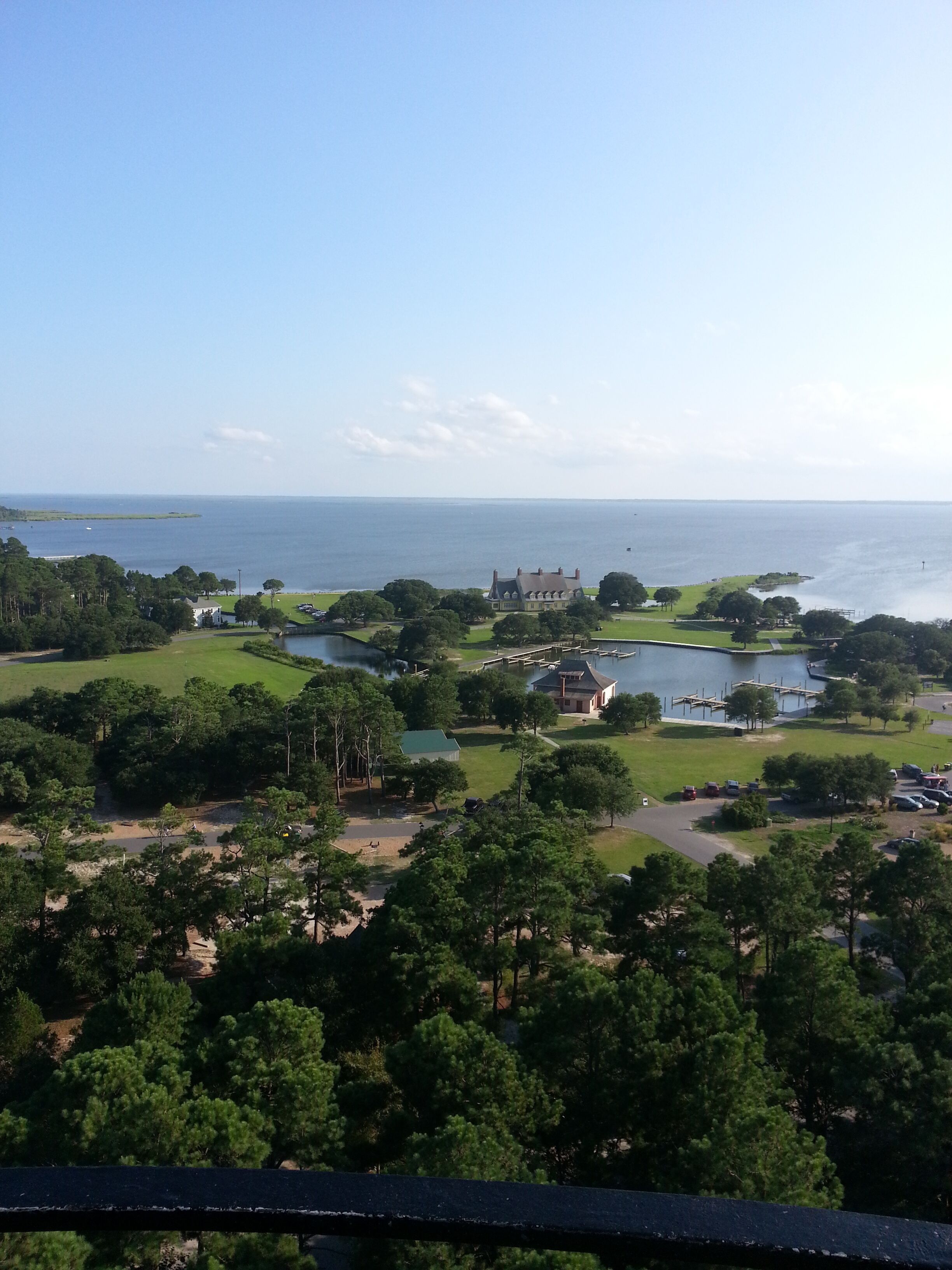 A coastal landscape with a large body of water, a golf course, and a prominent building with a distinctive roof.