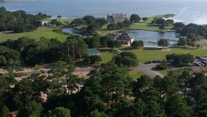 Kystlandskab med et stort vandområde, en golfbane og en markant bygning med et karakteristisk tag.