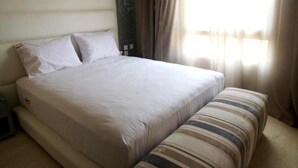 A neatly made bed with white linens, a bedside table, and a striped cushion. - Residence Genegelis 4055 (Marrakech)