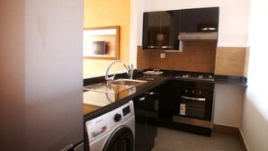 A compact kitchen with a washing machine, a built-in oven, and a microwave. - Residence Genegelis 4055 (Marrakech)