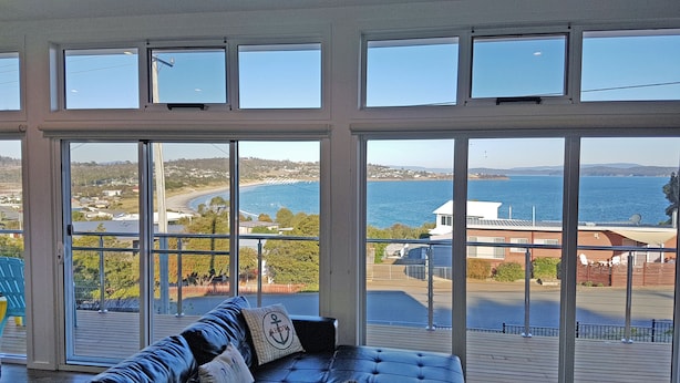Habitación con un amplio ventanal que da a la costa, un sofá de cuero y vistas al mar y edificios al fondo.