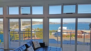 Une pièce dotée d’une grande fenêtre donnant sur la côte, d’un canapé en cuir et offrant une vue sur la mer et les bâtiments situés au loin.