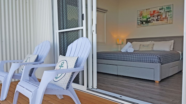 Une pièce comprenant un lit, deux chaises, une porte-fenêtre coulissante et un tableau accroché au mur.
