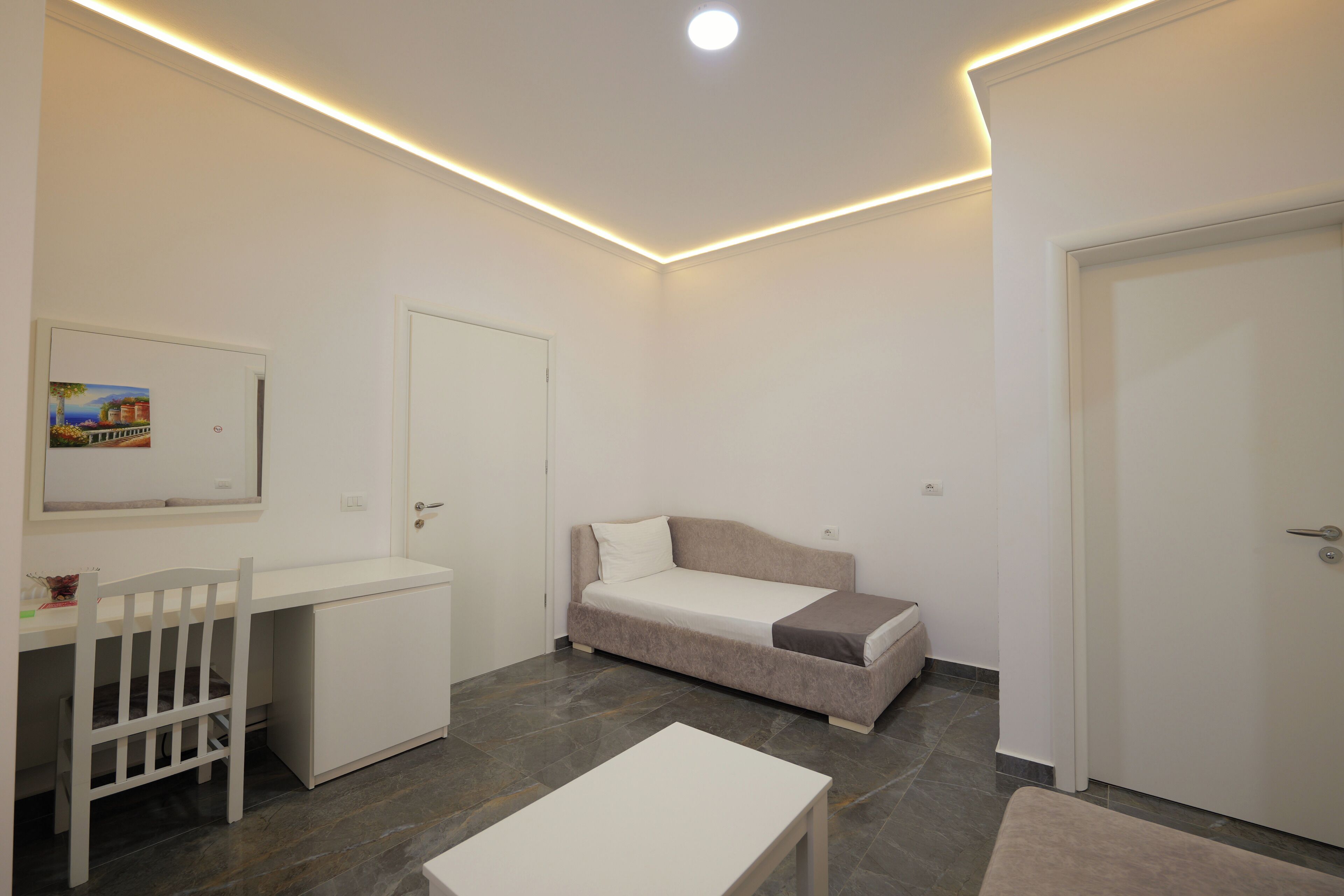 A small, modern room with a white desk, a bed, and a chair.