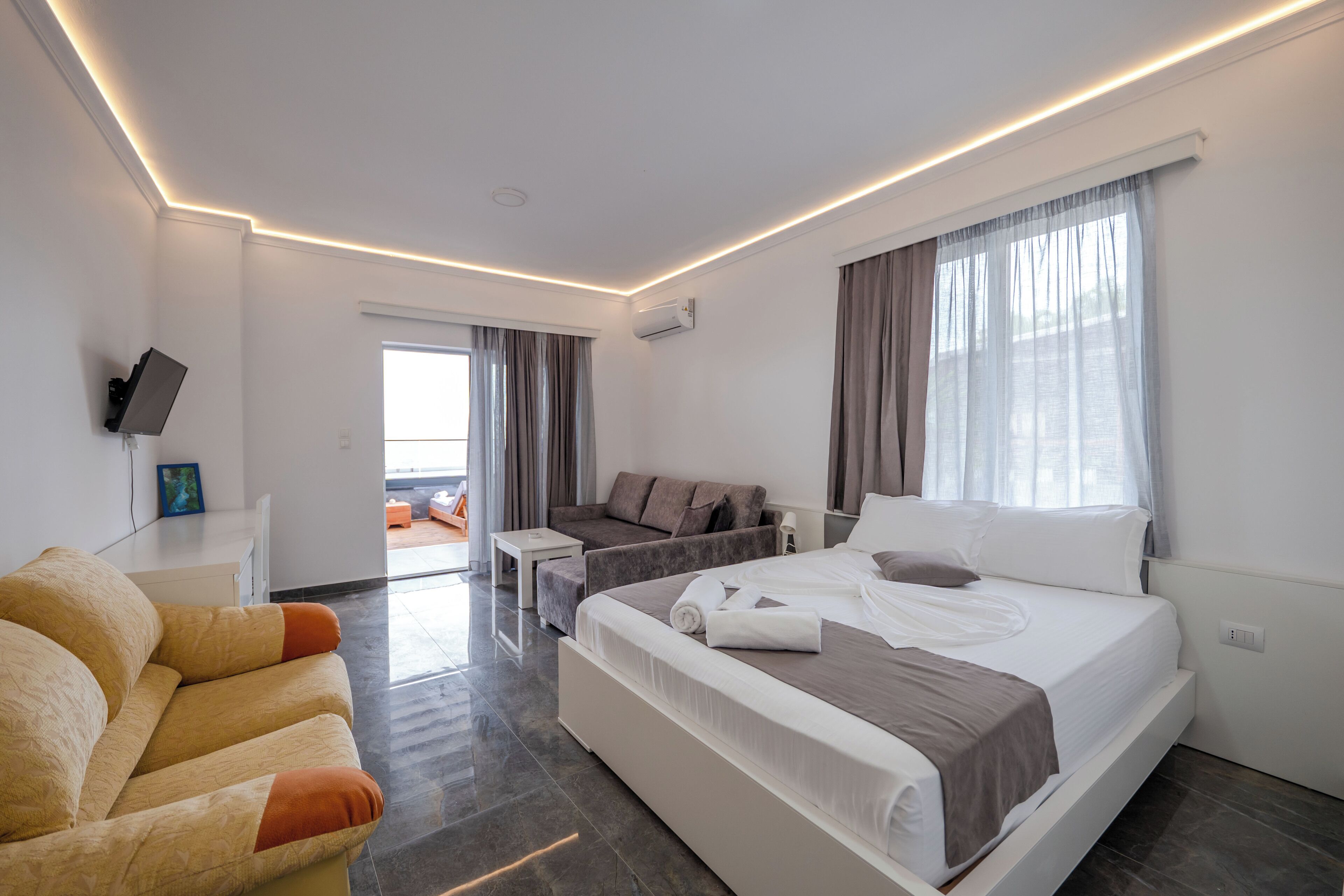 A modern hotel room with a large bed, a sofa, a small table, and a TV mounted on the wall.