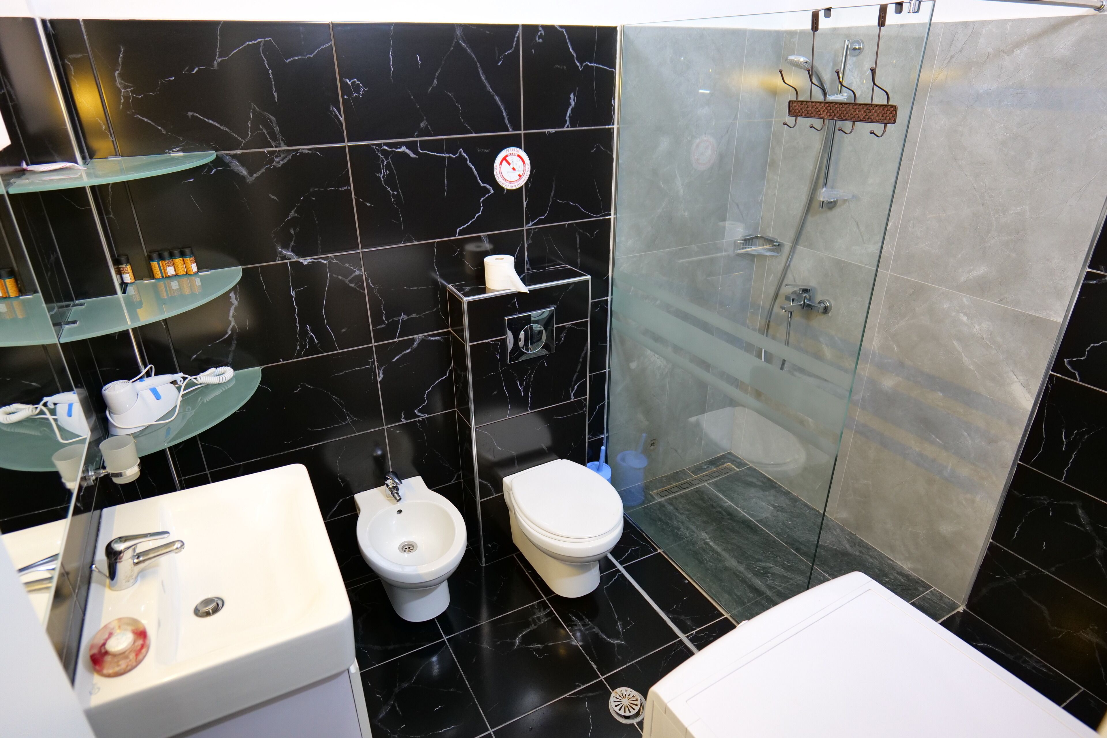A modern bathroom with a black marble backsplash, a glass shower enclosure, a sink with a bidet, and a toilet.