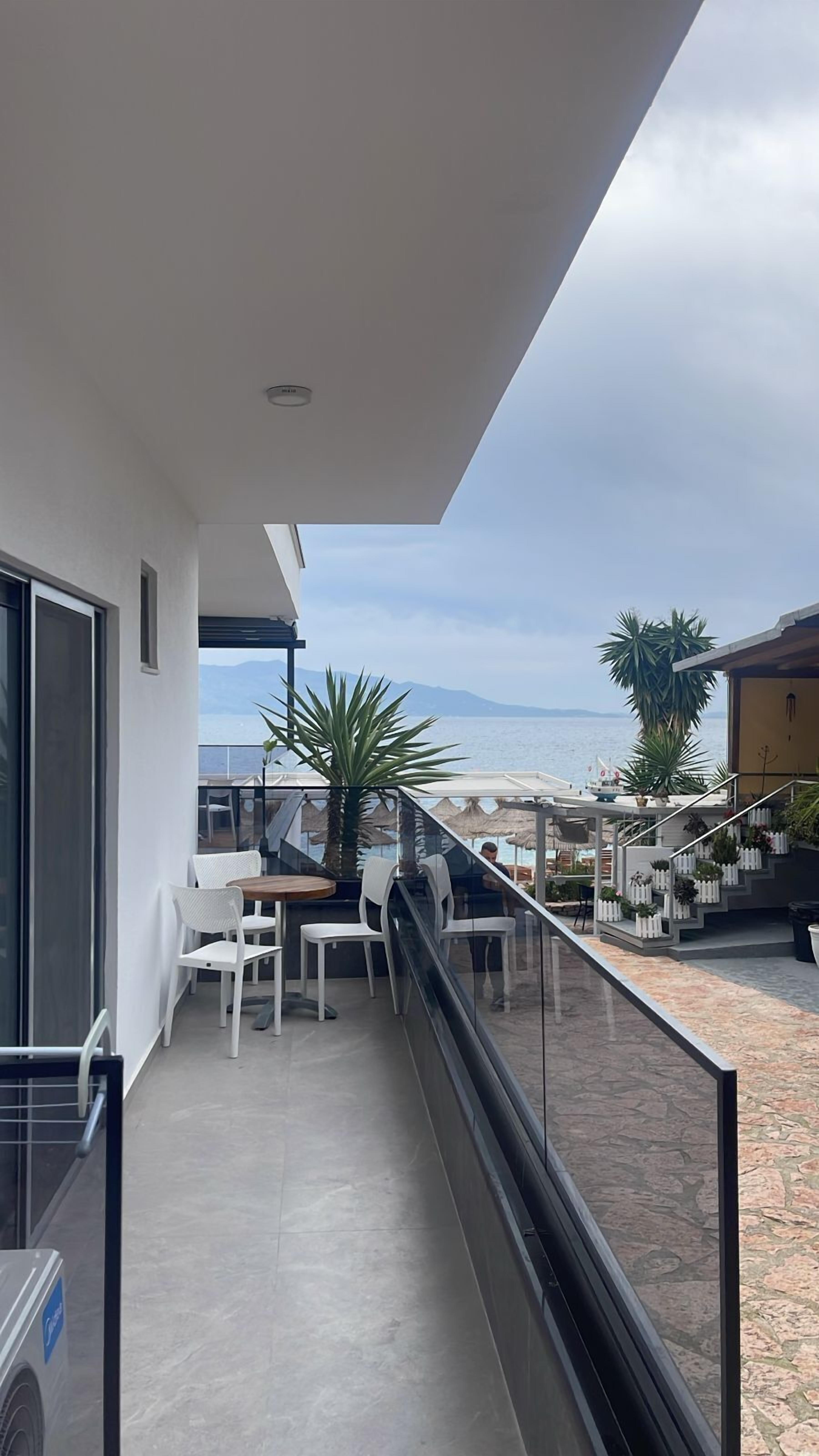 Ein Balkon mit Meerblick, weißen Stühlen, einem Tisch und einem Blumentopf.