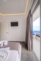 Una habitación de hotel moderna con una cama, un televisor de pantalla plana montado en la pared y un balcón con vista al mar.