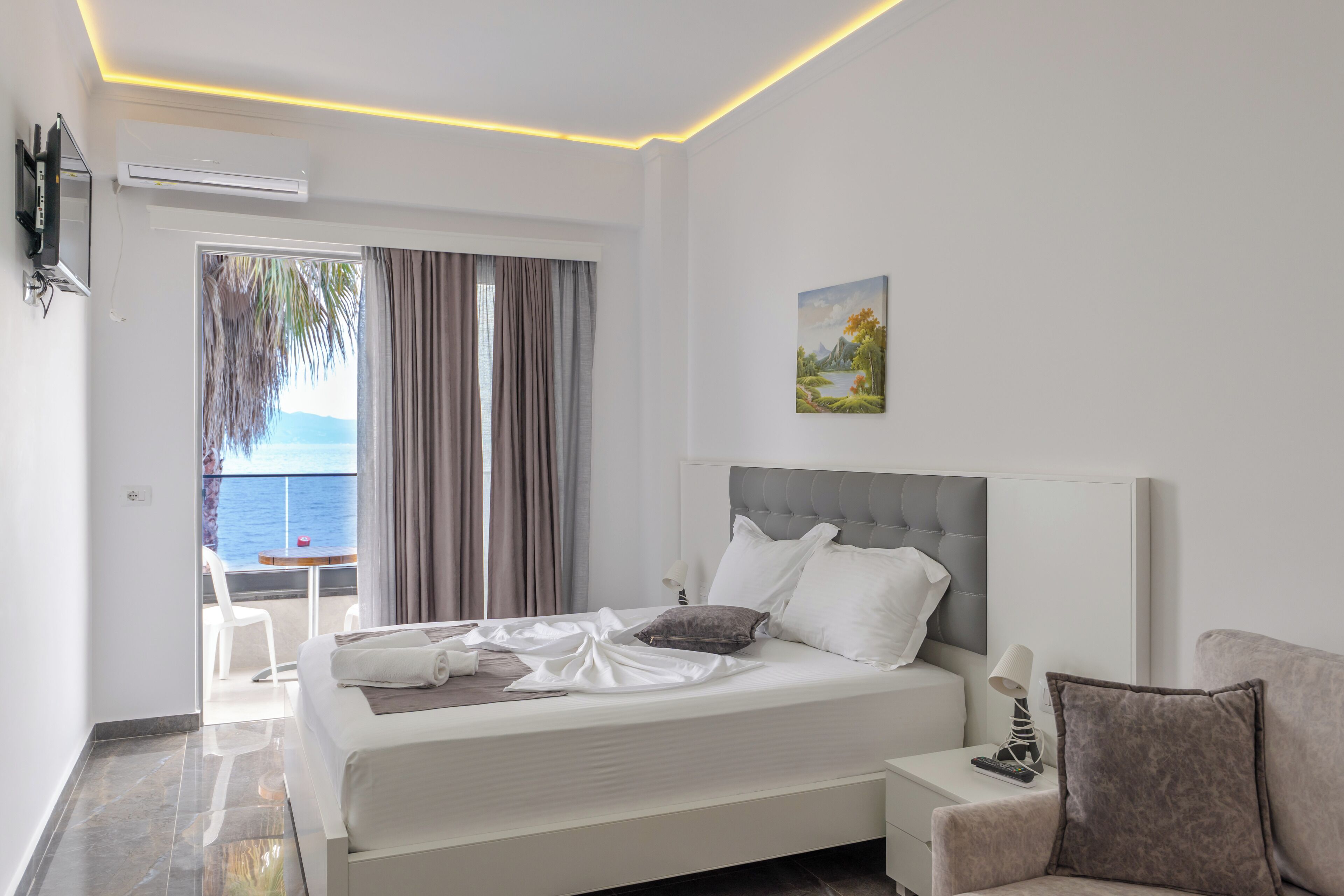 Habitació d'hotel moderna amb un llit gran, una taula de nit, una televisió i vista al mar.