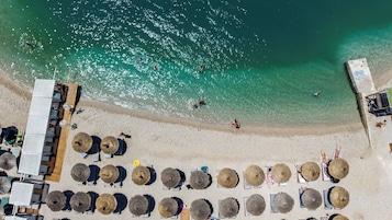 An aerial view of a beach with sun loungers, umbrellas, and a few people swimming in the water.
