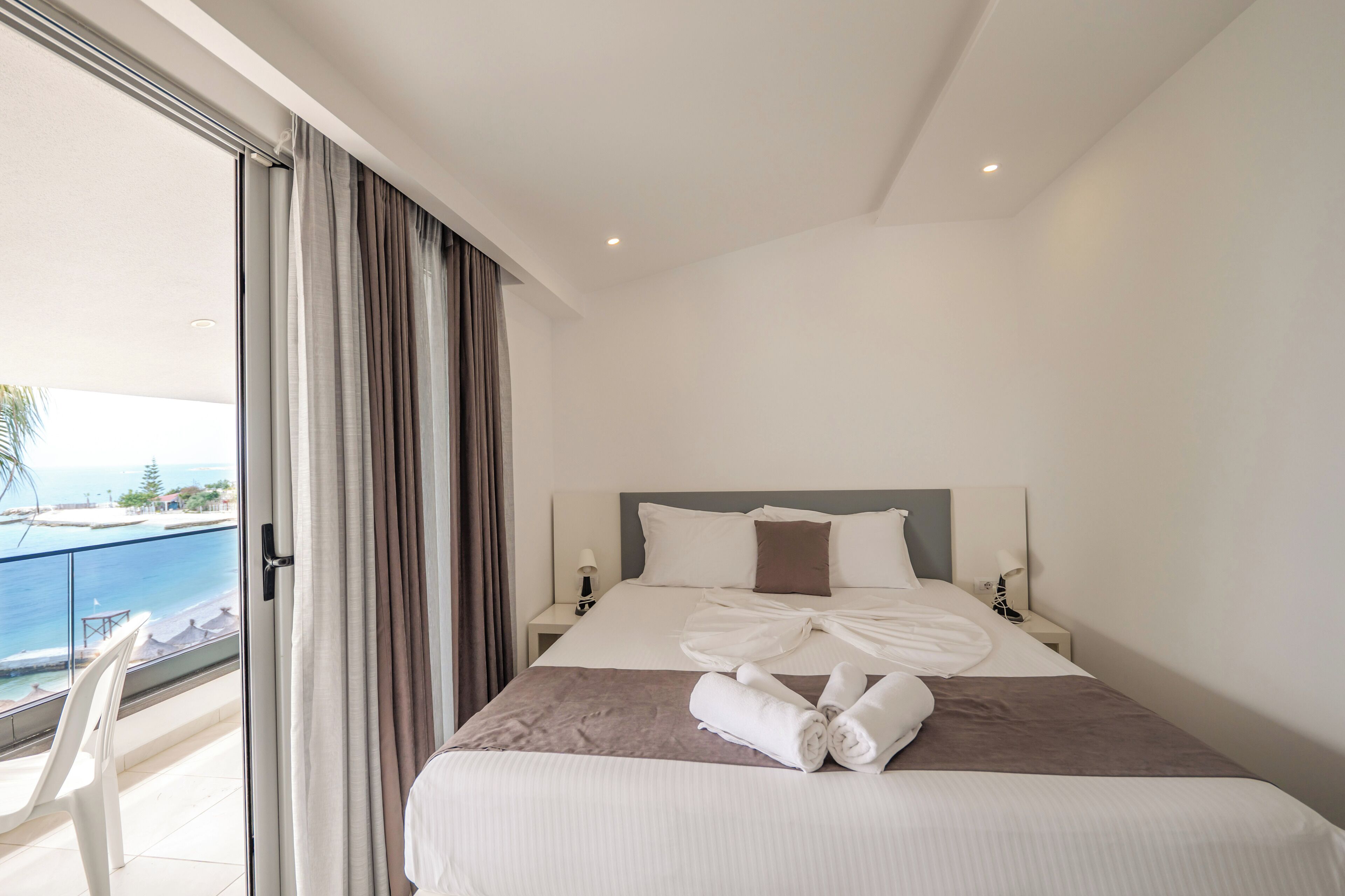 A hotel room with a bed, a nightstand, a lamp, and a view of the sea.