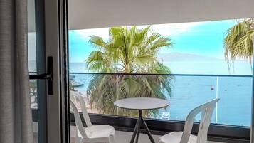 En balkon med to hvide plaststole og et lille rundt bord, med udsigt over en strand med palmer og havet.