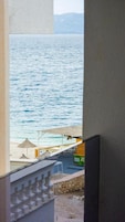 A view of the sea from a window overlooking a beach area with umbrellas and a small building.